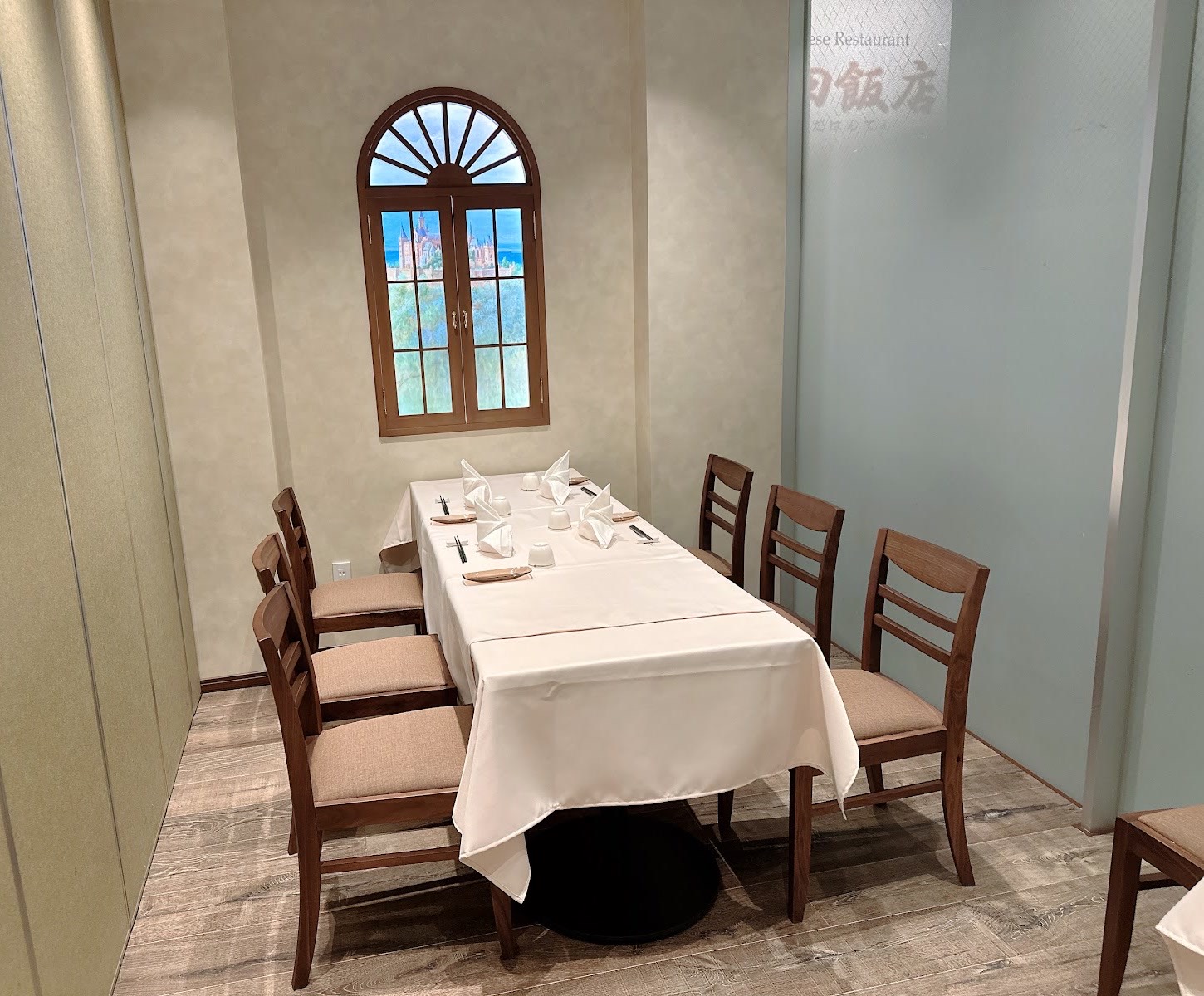 アーチ窓のある壁ぎわの六人掛けの白いテーブル。右のすりガラスに「…田飯店」の筆文字。