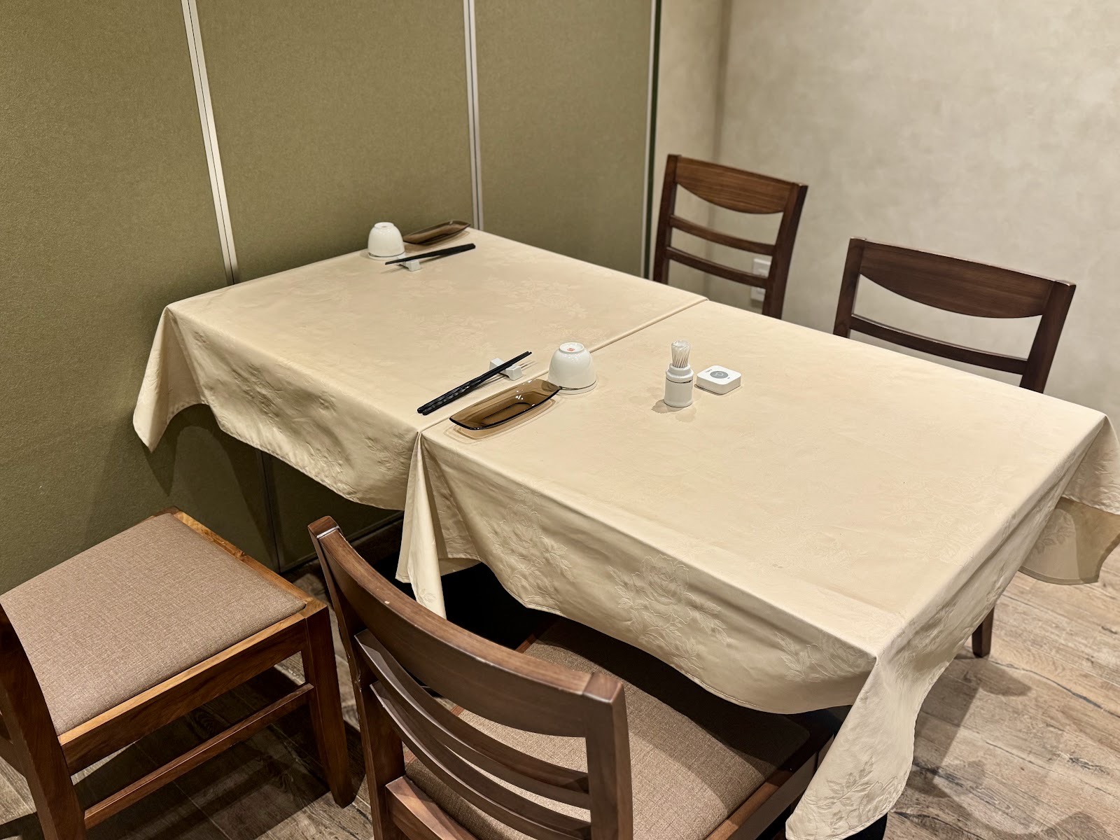 淡い色の間仕切りに囲まれた四人掛けのテーブル。白いクロス、箸と小さな白い器、木の椅子。