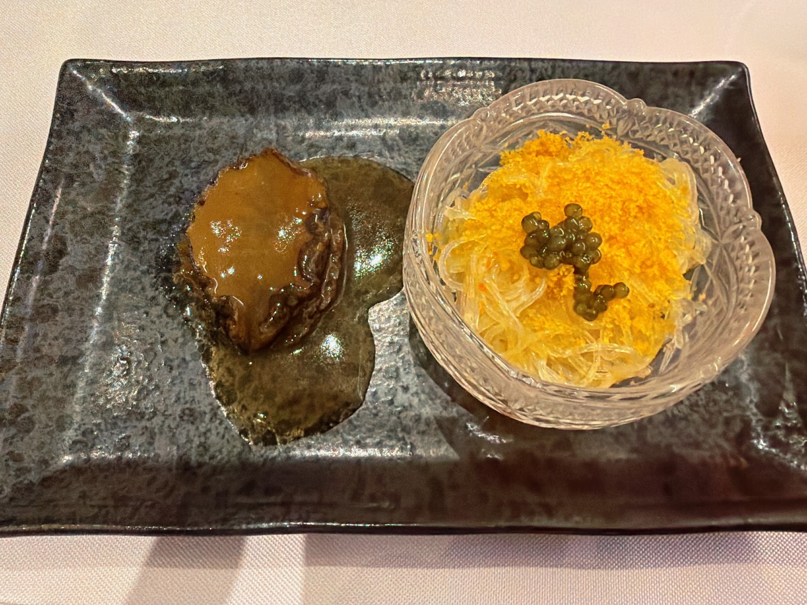 黒い石の皿に、とろみのあるソースの煮アワビと、オレンジ色の魚卵と黒い粒を載せた春雨。