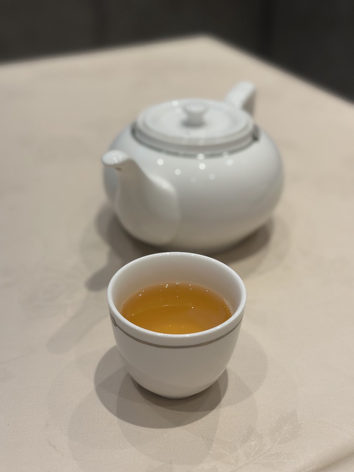 白いクロスの上の白い急須と、黄金色のお茶が入った小さな茶碗。